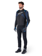 Alpinestars T-Jaws V4 vandtæt jakke, sort, mørkeblå og Blithe Blue, båret af en model med sorte motorcykelbukser og kørestøvler, hvidt Alpinestars-logo på brystet og blå skulderdetaljer, sport-fit køreudstyr