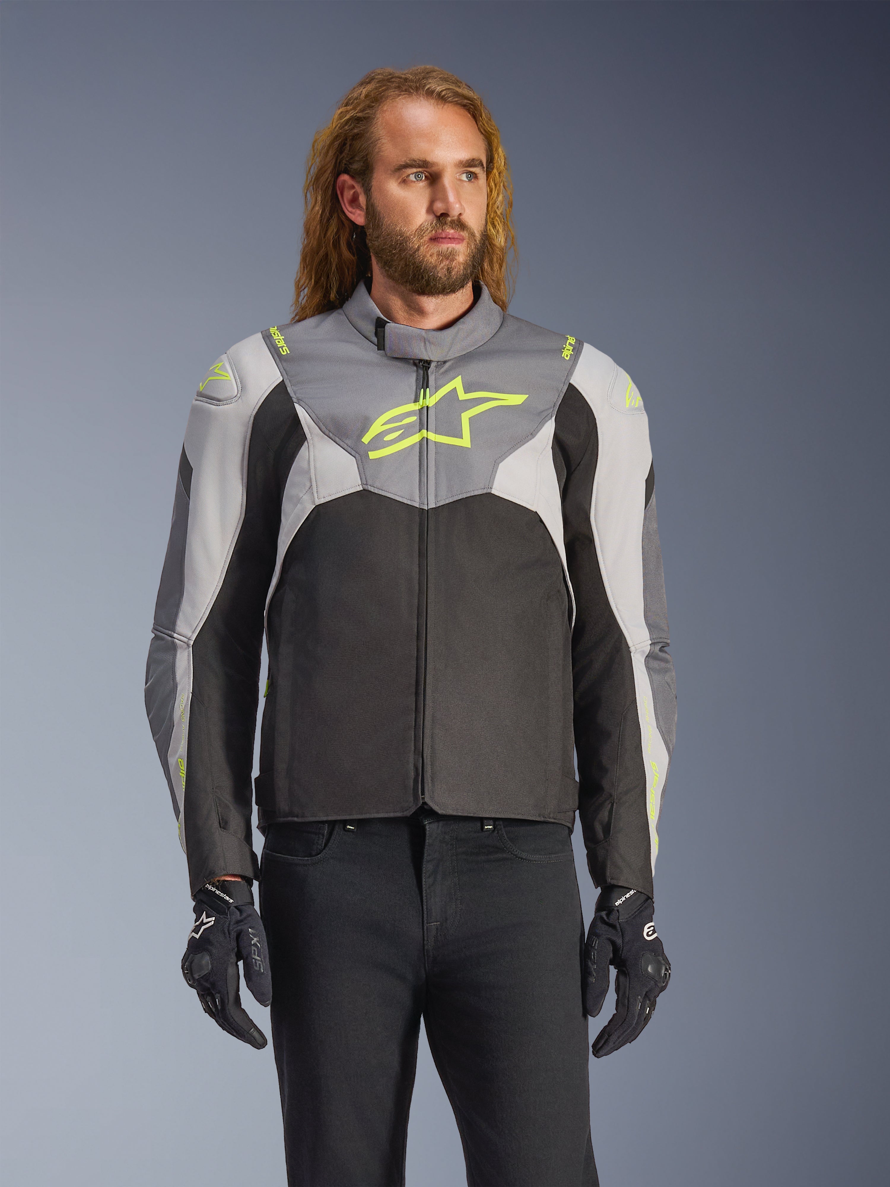 Alpinestars T-Jaws V4 vandtæt jakke båret af en mandlig model, Black Ice Gray og mørkegrå med neongule detaljer, med et fremtrædende gult stjernelogo på brystet, stylet med sorte bukser og kørehandsker, sport-fit tekstil-motorcykeljakke