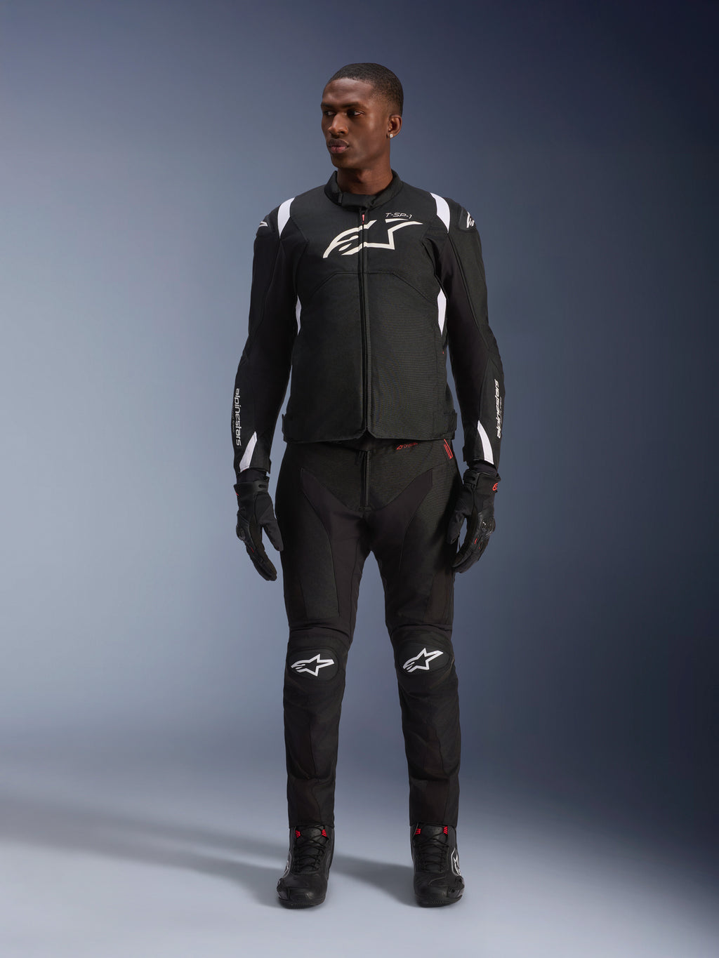 Alpinestars T-SP 1 V2 vandtæt jakke, sort og hvid, med et markant hvidt logo på brystet og detaljer på skuldrene, båret med matchende sorte motorcykelbukser og handsker for et komplet road riding-look
