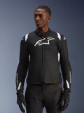 Alpinestars T-SP 1 V2 vandtæt jakke, motorcykeljakke i sportstekstil, sort og hvid med diskrete røde detaljer, båret af en mandlig model med matchende handsker og bukser, med hvidt Alpinestars-logo på brystet, T-SP-1-branding og beskyttende silhuet til landevejskørsel
