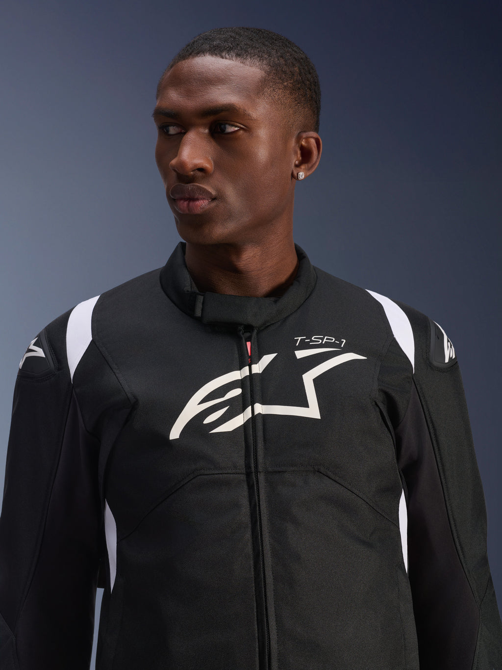 Alpinestars T-SP 1 V2 Vandtæt Jakke bæres af en model, sort og hvid tekstil motorcykeljakke, stort hvidt Alpinestars-logo og T-SP-1-branding på brystet, sporty design med beskyttende skulderslidere