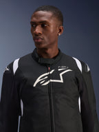 Alpinestars T-SP 1 V2 Vandtæt Jakke bæres af en model, sort og hvid tekstil motorcykeljakke, stort hvidt Alpinestars-logo og T-SP-1-branding på brystet, sporty design med beskyttende skulderslidere