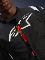 Alpinestars T-SP 1 V2 vandtæt jakke, sort og hvid, med et stort hvidt brystlogo og 'T-SP-1'-tekst, orange indvendig flap med 'Alpinestars Protects'- og 'Tech-Air Ready'-branding, slidstærkt motorcykeludstyr i tekstil