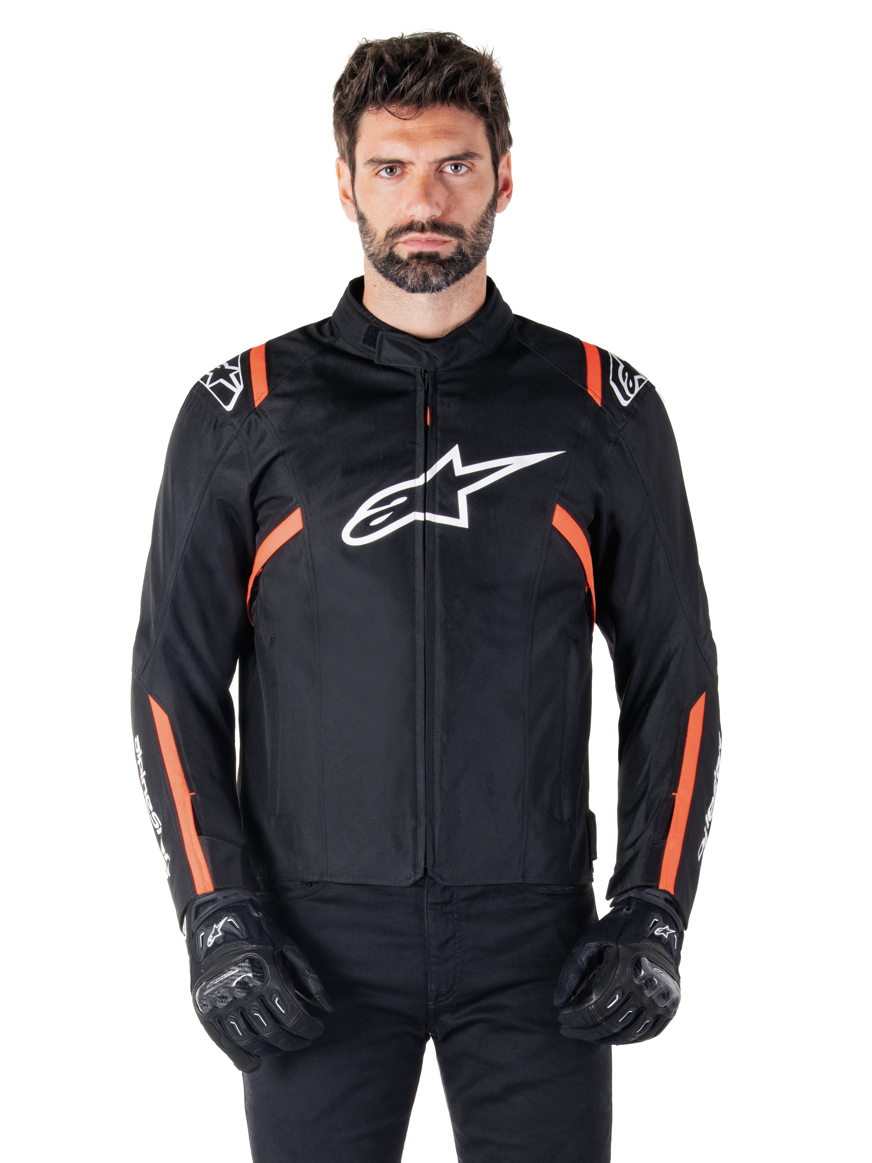 Alpinestars T-SPS V2 Waterproof Jacket, Black White and Red Fluo, worn by a male model with black riding gloves, featuring a large white Alpinestars logo on the chest and vibrant orange accents on the shoulders and sleeves.