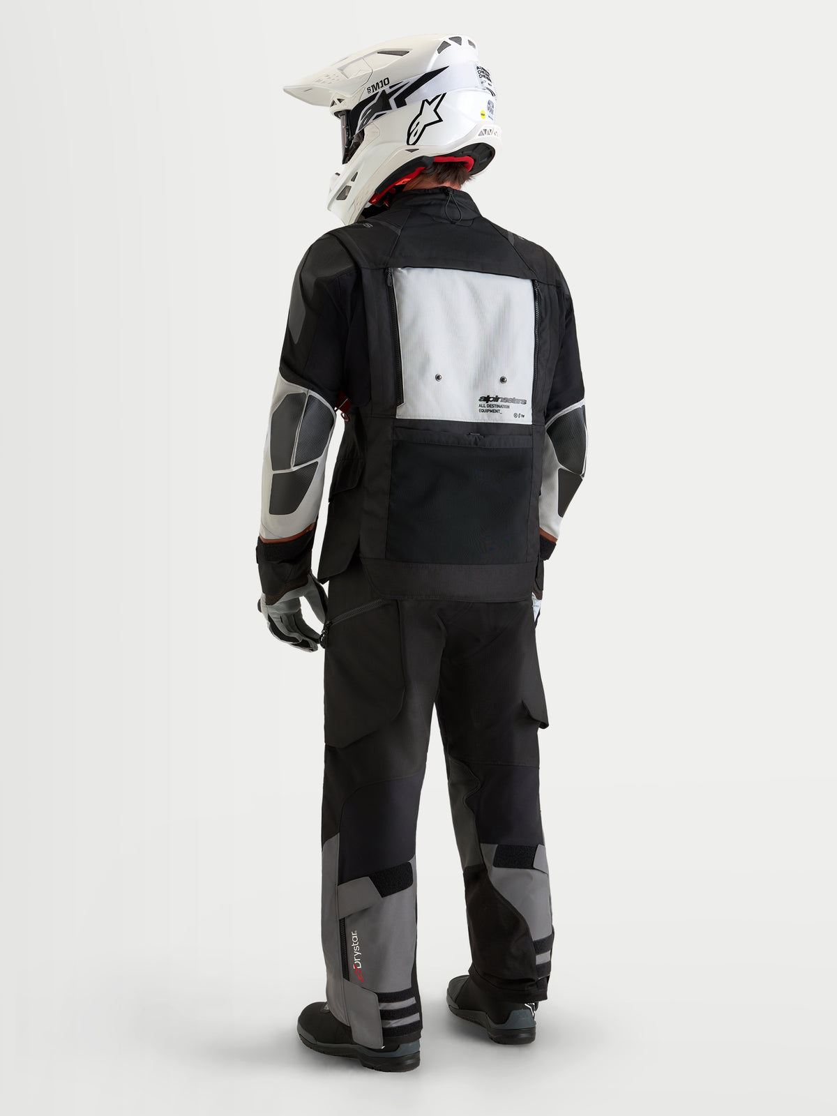 Alpinestars Harok V2 Drystar jakke, herre adventure motorcykeljakke, mørkegrå, isgrå og sort, set bagfra med modulær ventilationspanel, PU-forstærkningszoner og matchende adventure-bukser samt hvid offroad-hjelm