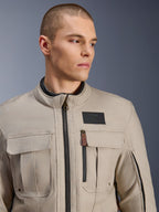Mandlig model iført Alpinestars Borrego Drystar® jakke i Warm Gray, adventure-motorcykeljakke med et klassisk vokset-lærred look, funktionelle brystlommer i cargostil og et sort Alpinestars-logomærke.