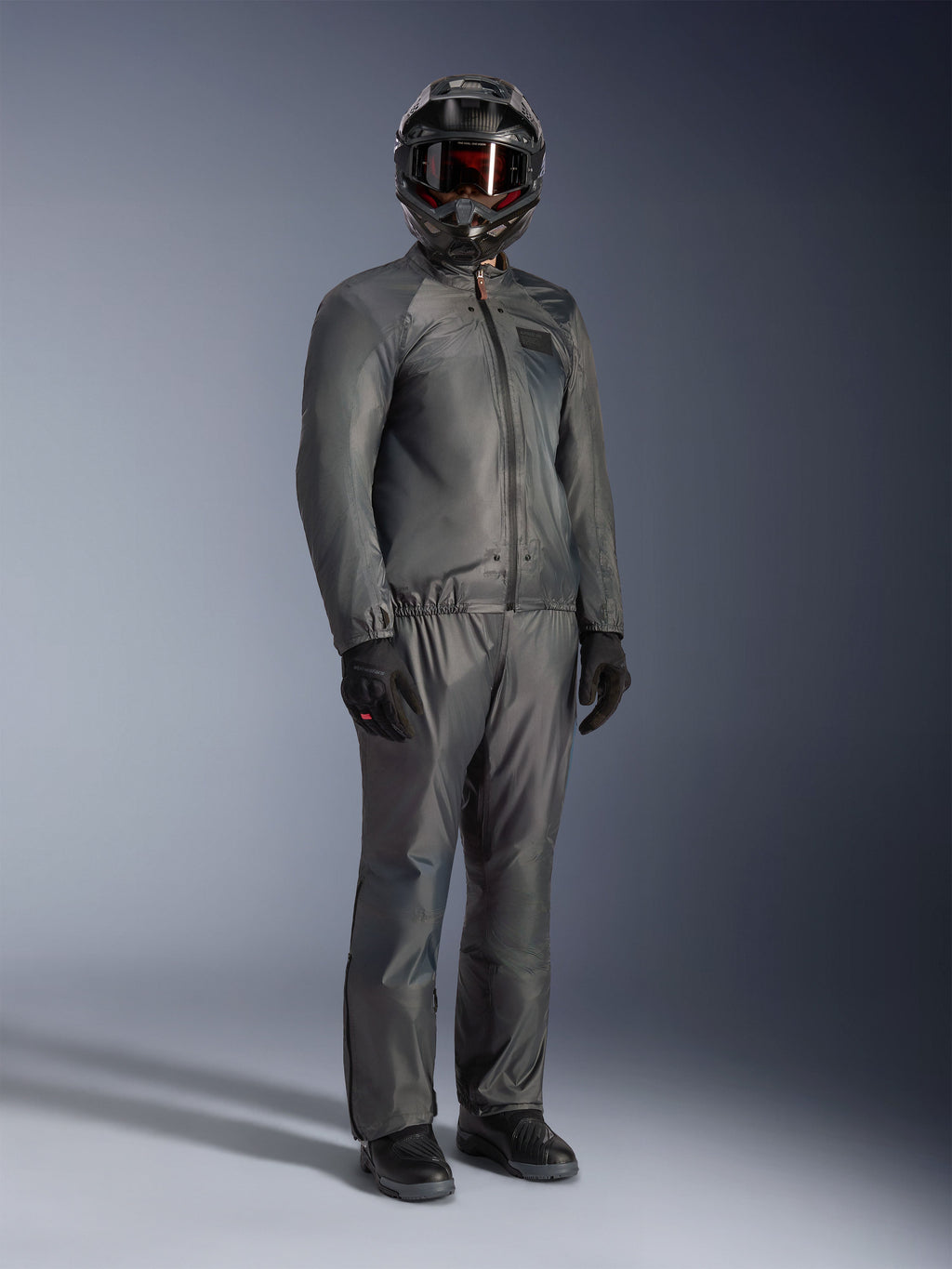 Rytter iført Alpinestars Borrego Drystar®-jakke i Warm Gray, komplet adventure-udstyr med matchende grå bukser, sort full-face-hjelm med goggles og sorte handsker, med et stilrent vandtæt tekstildesign.