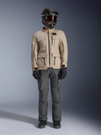 Alpinestars Borrego Drystar® jakke i Warm Gray, adventure motorcykeljakke med fire cargo-lommer foran, kombineret med mørkegrå kørebukser, sort off-road hjelm og sorte handsker, med et robust voksbehandlet lærredslook
