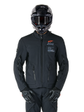 Alpinestars AMT-8 Stretch Drystar® XF-jakke, sort motorcykeljakke, med orange Alpinestars-logo og grå AMT-branding, høj krave med lynlås foran og ventilationsåbninger, bæres med sort hjelm og handsker, beskyttende adventure touring-udstyr
