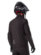 Alpinestars AMT-8 Stretch Drystar® XF-liner, sort vandtæt jakkeliner, set bagfra på en kører iført sort hjelm og handsker, med Alpinestars Motion Technology-branding på lænden, minimalistisk og funktionelt design til adventure-kørsel.