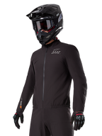 Motorcyklist iført Alpinestars AMT-8 Stretch Drystar® XF Liner, sort vindtæt og vandtæt strækjakke med AMT-logo på brystet og Drystar XF-branding på ærmet, kombineret med en sort adventure-hjelm og beskyttelseshandsker.