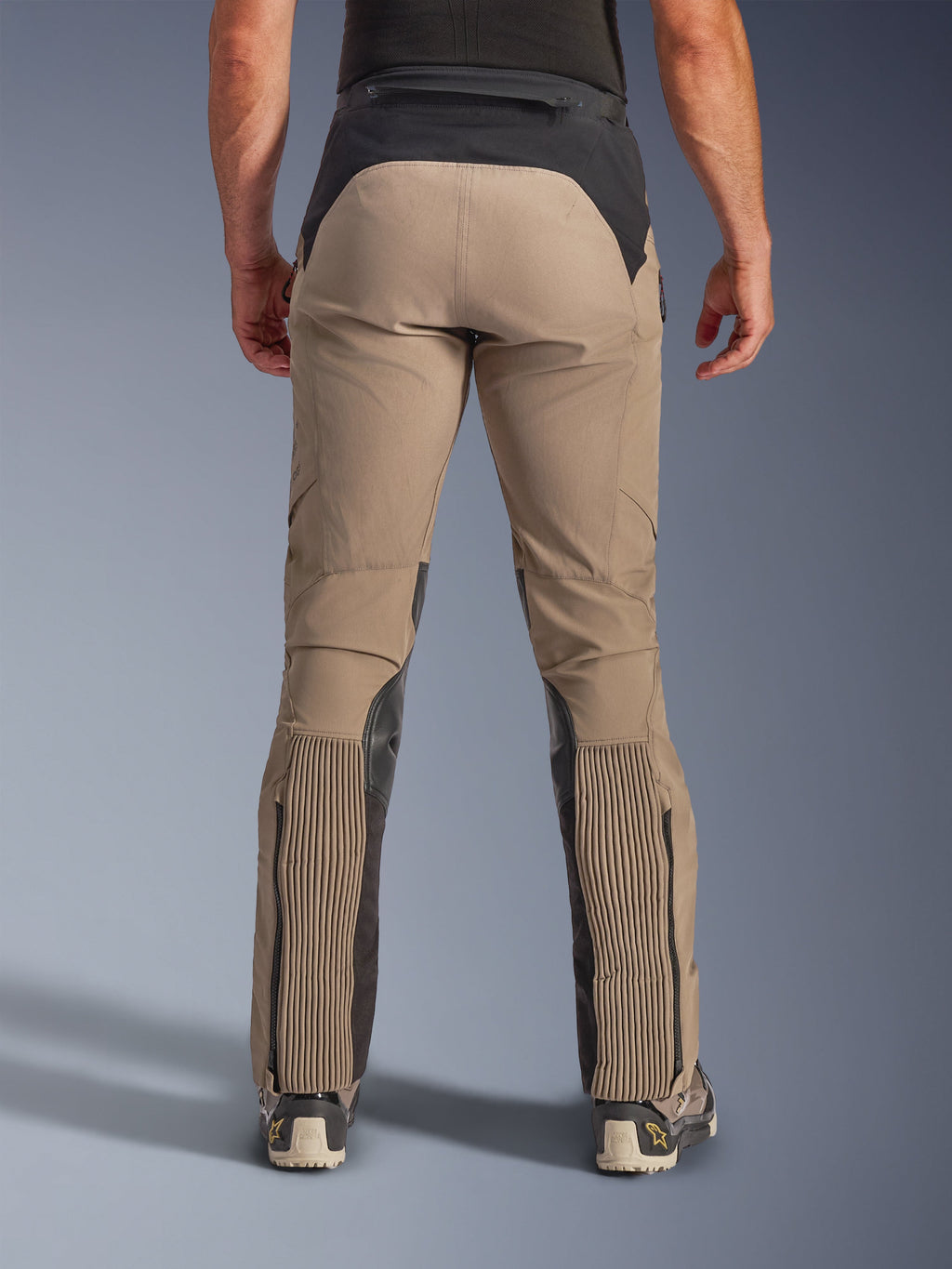 Alpinestars AMT-8 Stretch Drystar® XF bukser, Walnut Black, set bagfra på model, tanfarvet stræktekstil med sorte paneler på talje og lægge, store harmonika-stræksektioner på underbenene, benåbninger med lynlås og adventure-touring pasform