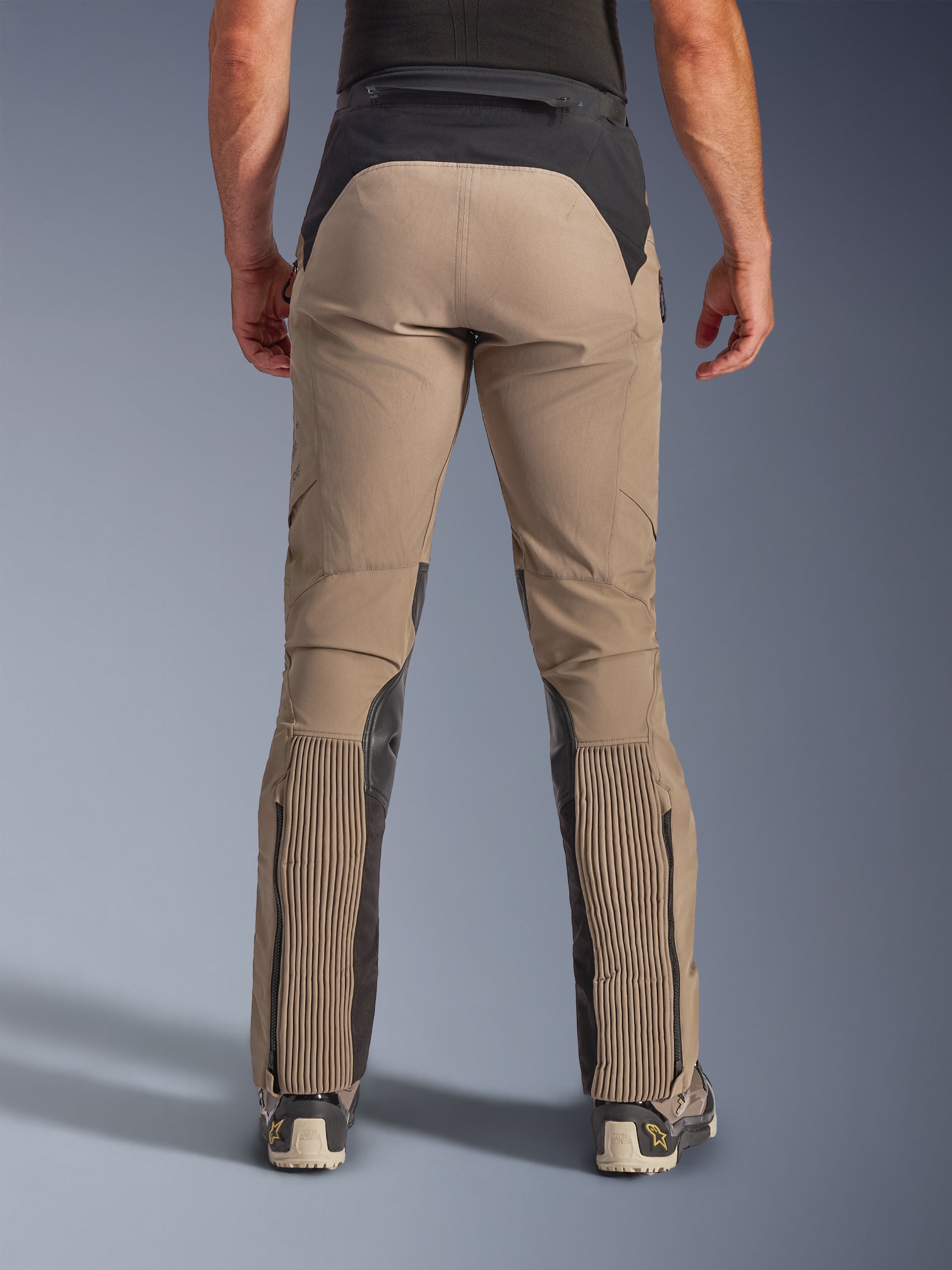 Alpinestars AMT-8 Stretch Drystar® XF bukser, Walnut Black, set bagfra på model, tanfarvet stræktekstil med sorte paneler på talje og lægge, store harmonika-stræksektioner på underbenene, benåbninger med lynlås og adventure-touring pasform