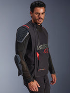 Alpinestars Halo Pro Drystar® XF lamineret jakke, Black og Dark Shadow, adventure-motorcykeljakke båret af model, modulær konfiguration med mesh-ærmer og integreret skulder- og albuebeskyttelse, røde logodetaljer og tekniske vandtætte lynlåse.