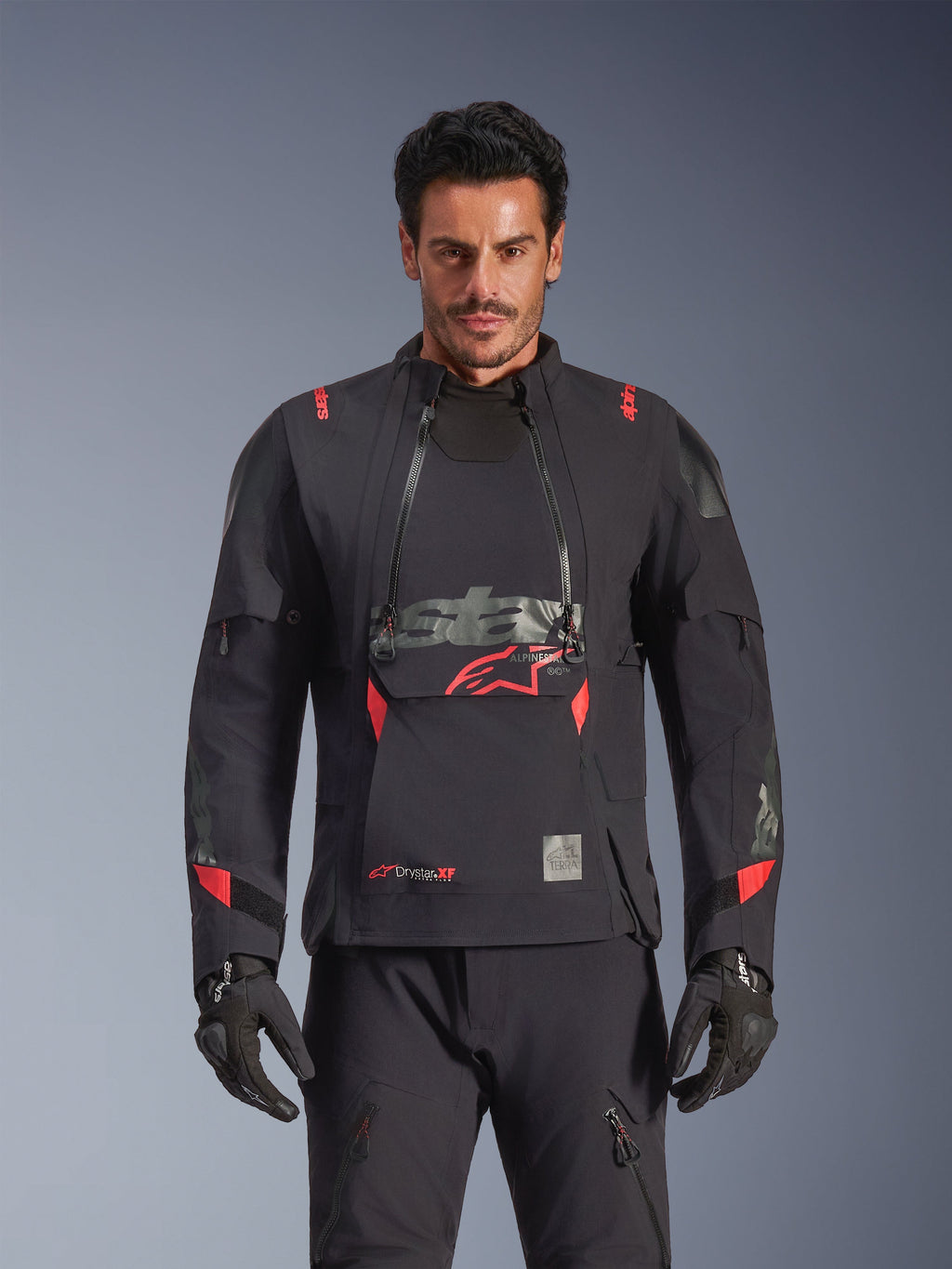 Alpinestars Halo Pro Drystar® XF lamineret jakke, adventure-motorcykeljakke, Black Dark Shadow med røde detaljer, mandlig model iført komplet teknisk udstyr inklusiv matchende handsker og bukser, set forfra der fremhæver modulære brystventilationspaneler og vandtæt konstruktion.