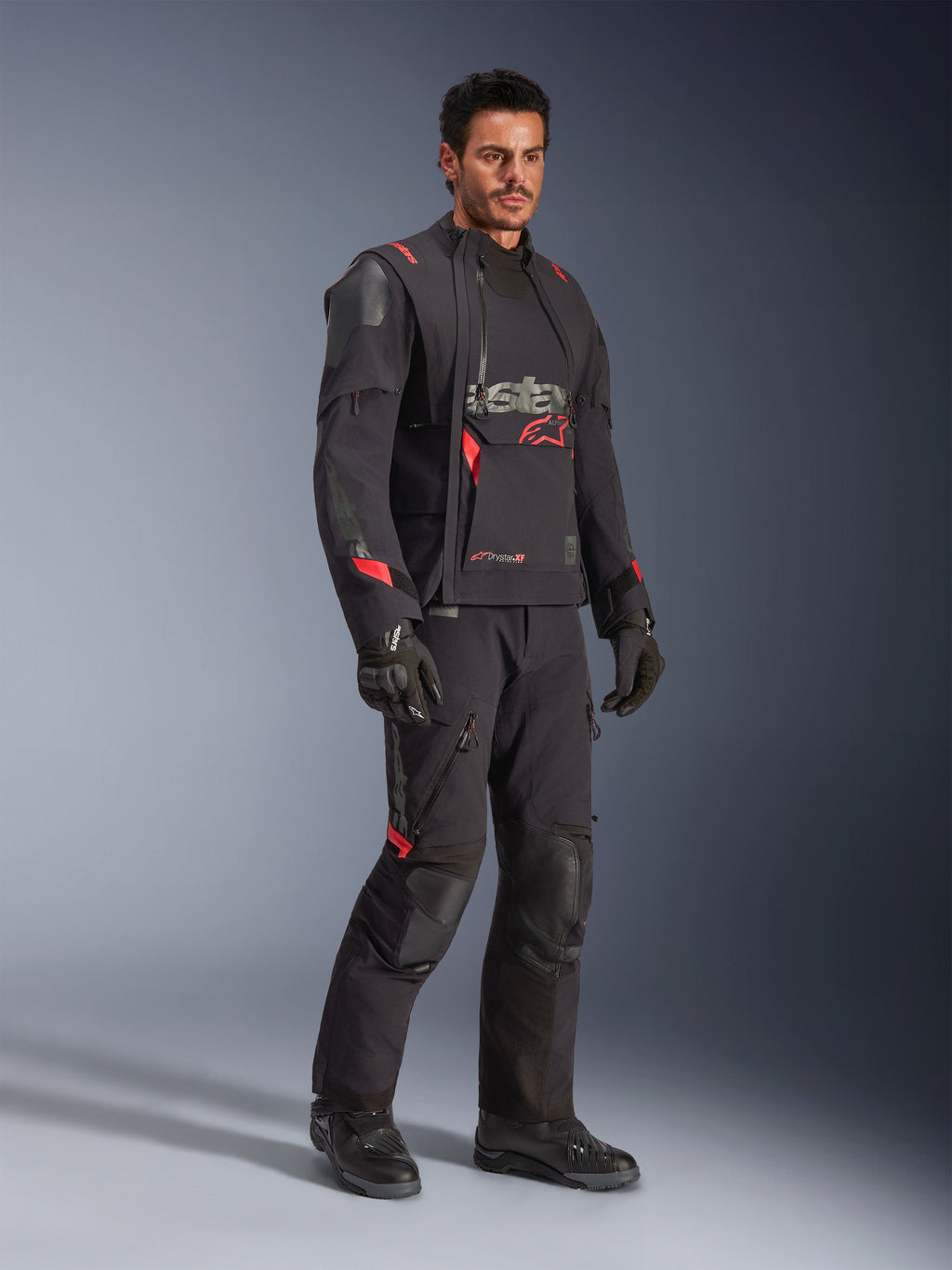 Mandlig kører iført Alpinestars Halo Pro Drystar® XF lamineret jakke i Black Dark Shadow, komplet adventure-køreudstyr med matchende bukser, handsker og støvler, med modulære asymmetriske frontpaneler og røde branding-detaljer.