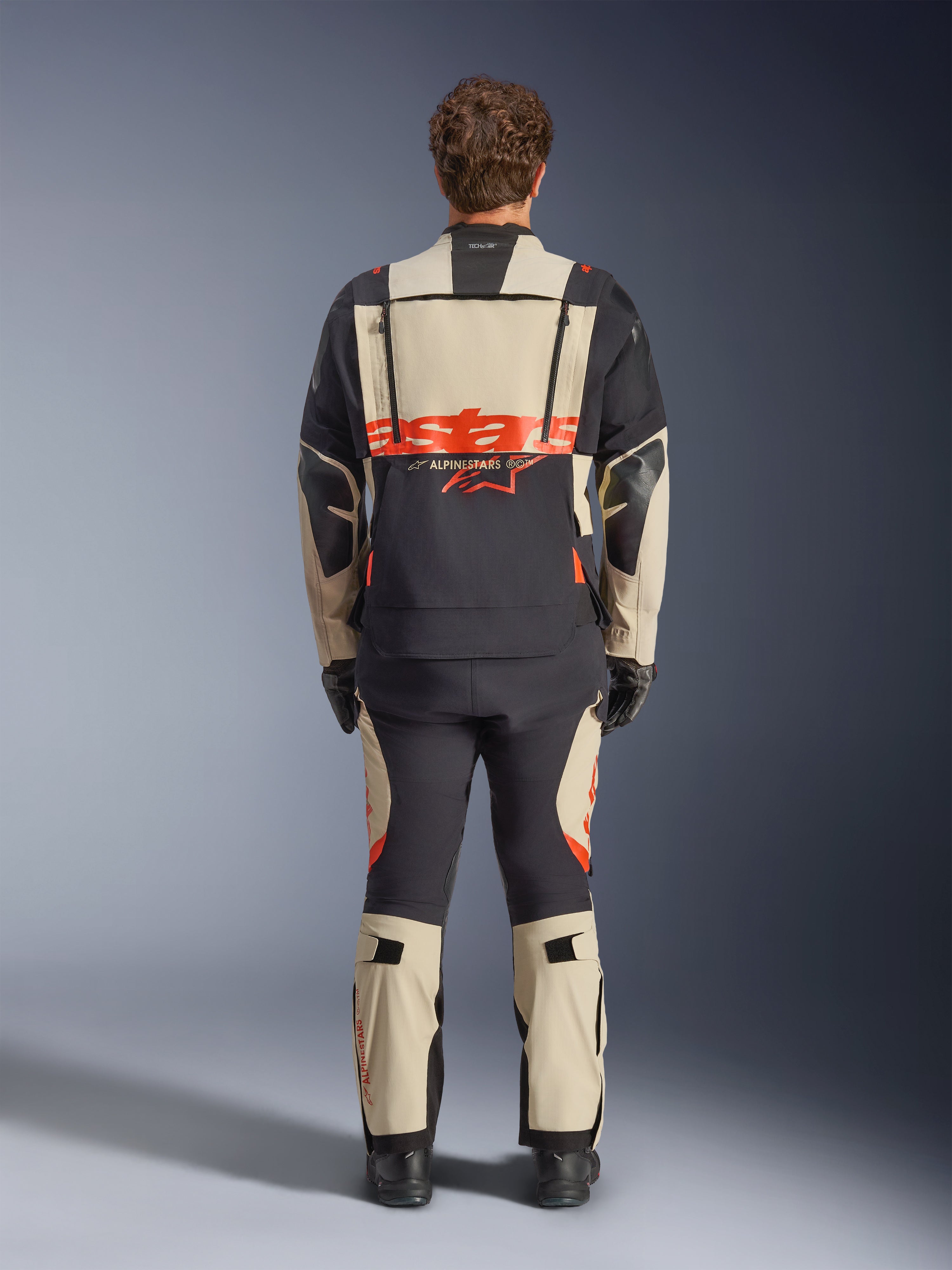Alpinestars Halo Pro Drystar® XF lamineret jakke, adventure motorcykeljakke, Mastic Black med orange logo, set bagfra med stor branding på ryggen og modulære ventilationslynlåse, båret med matchende adventure-bukser til terrænkørsel