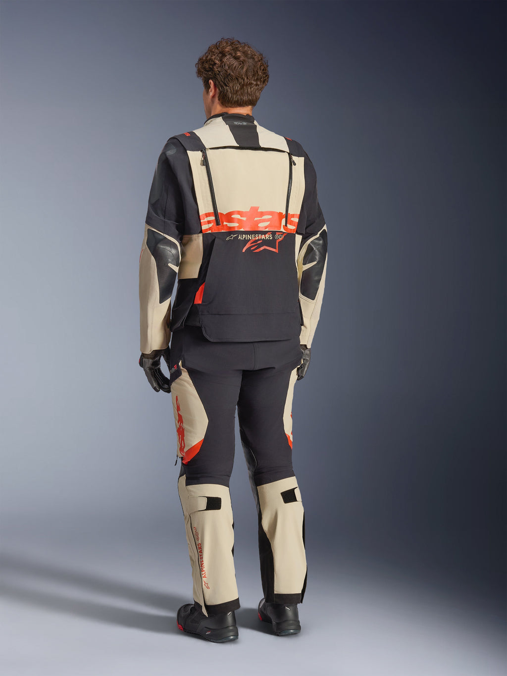 Alpinestars Halo Pro Drystar® XF lamineret jakke, Mastic Black, set bagfra, adventure motorcykeljakke med stort orange 'astars' branding over ryggen, båret med matchende tekniske bukser og støvler, modulært design til alsidigt terræn