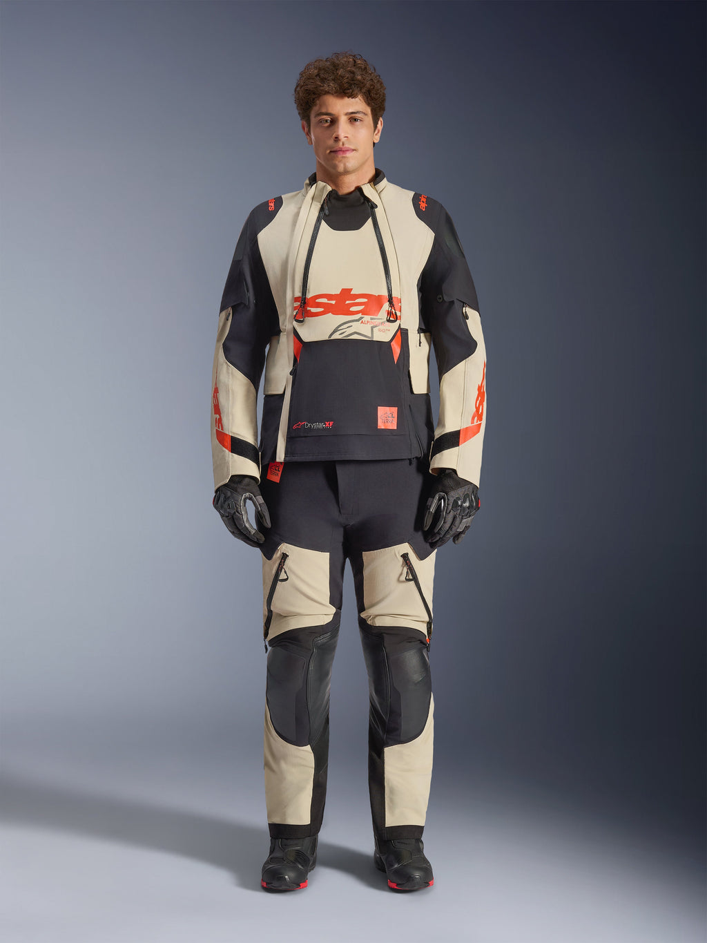 Alpinestars Halo Pro Drystar® XF lamineret jakke, Mastic Black, adventure-motorcykeljakke båret af en model med matchende bukser og handsker, sandfarvede og sorte tekstilpaneler med markante røde logoer, modulært design til kørsel i alt terræn