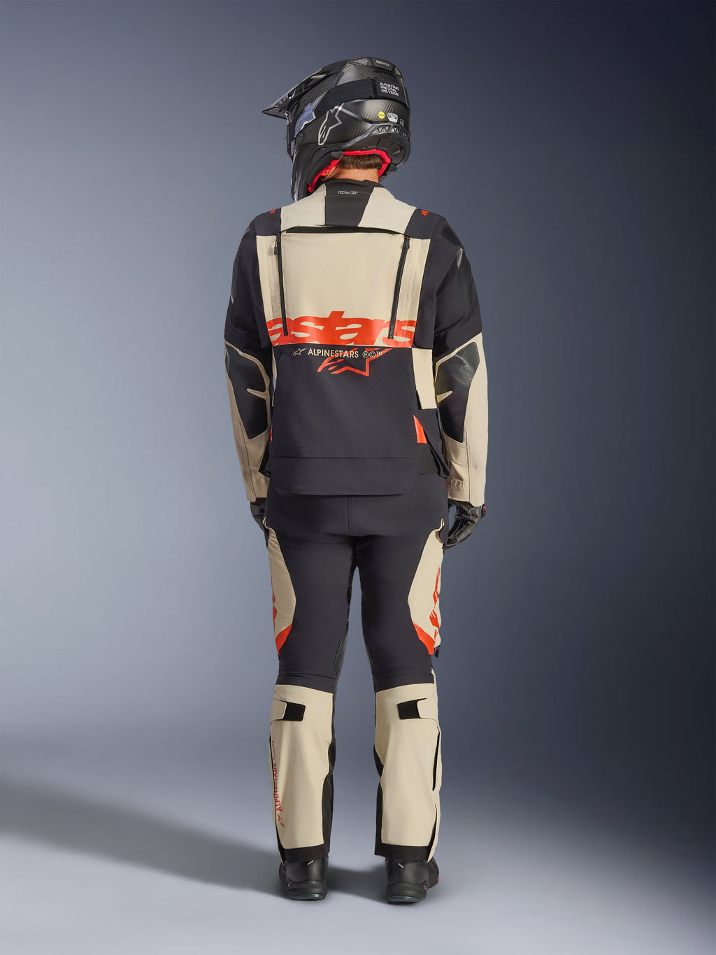 Alpinestars Halo Pro Drystar® XF lamineret jakke, adventure motorcykeljakke, Mastic Black, set bagfra af en kører med matchende bukser og sort hjelm, med markant orange Alpinestars-branding og modulære ventilationspaneler til alsidig eventyrkørsel