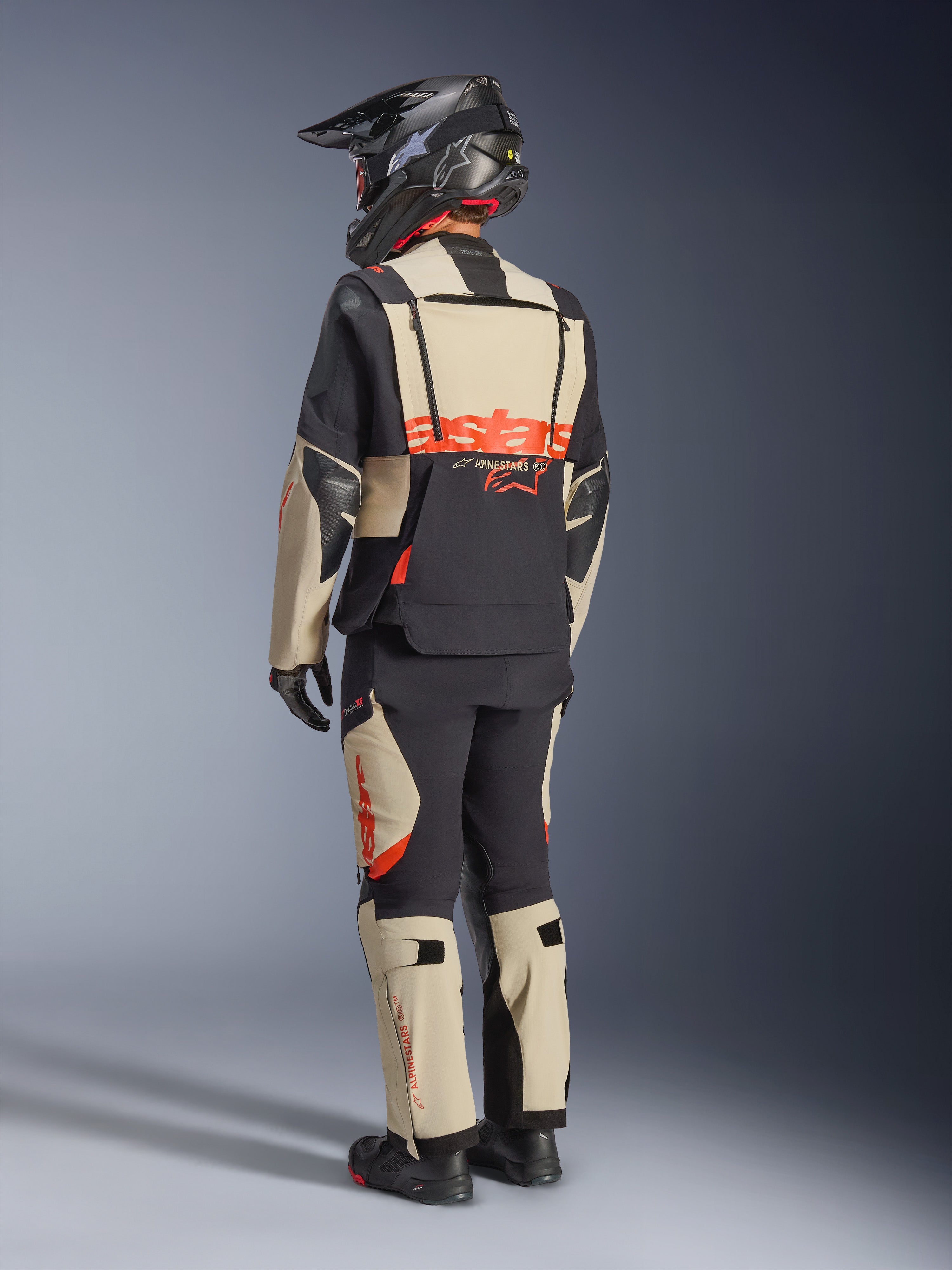 Alpinestars Halo Pro Drystar® XF lamineret jakke, Mastic Black, set bagfra af en kører iført den fulde adventure-motorcykeldragt med matchende bukser, sort adventure-hjelm og støvler, med et markant rødt Alpinestars-logo hen over ryggen.