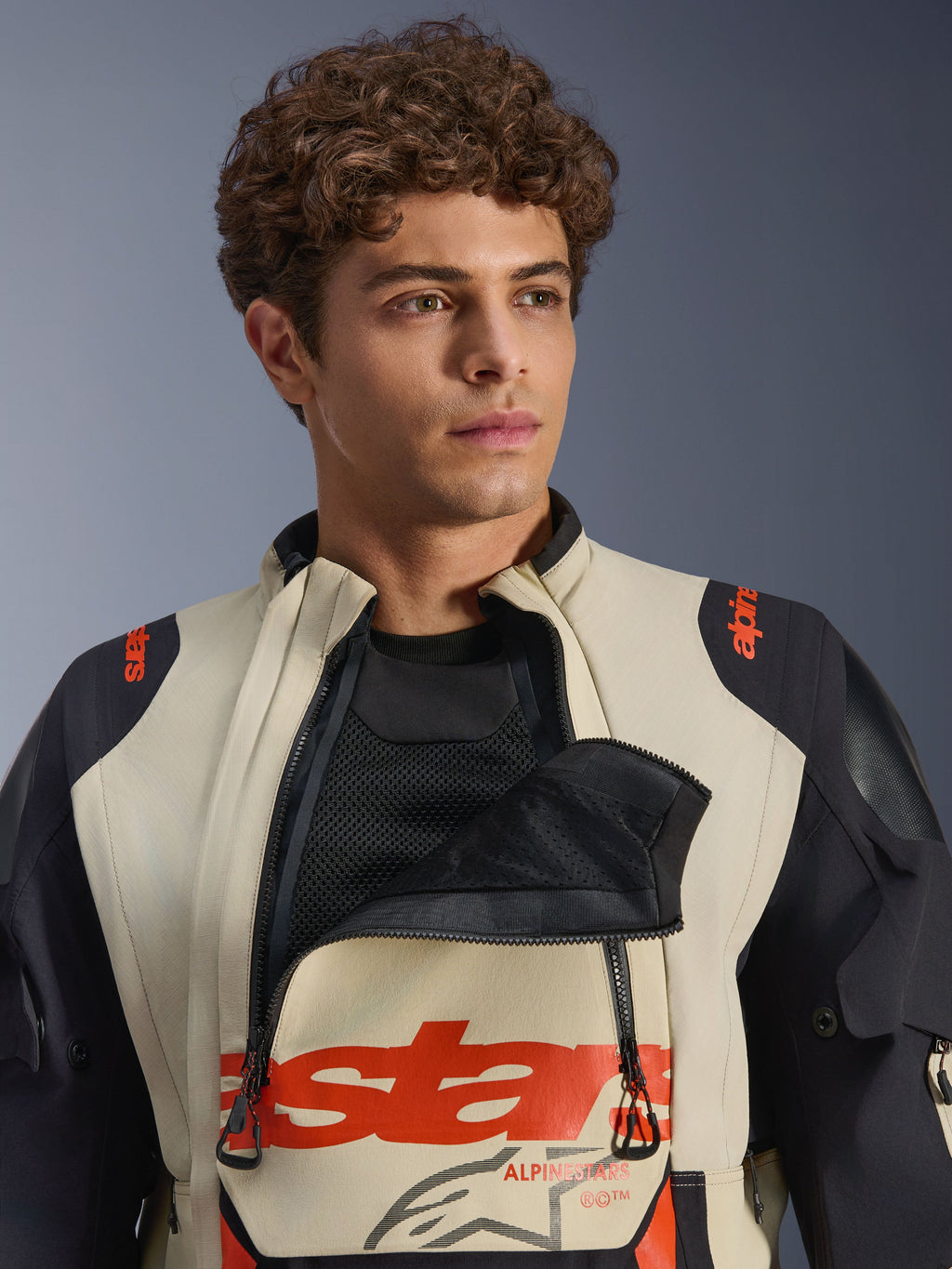 Alpinestars Halo Pro Drystar® XF lamineret jakke i Mastic Black, mandlig model iført jakken med brystventilationspanelet lynet ned for at vise mesh-underlaget, rød branding og sorte skulderpaneler, teknisk adventure-motorcykeludstyr