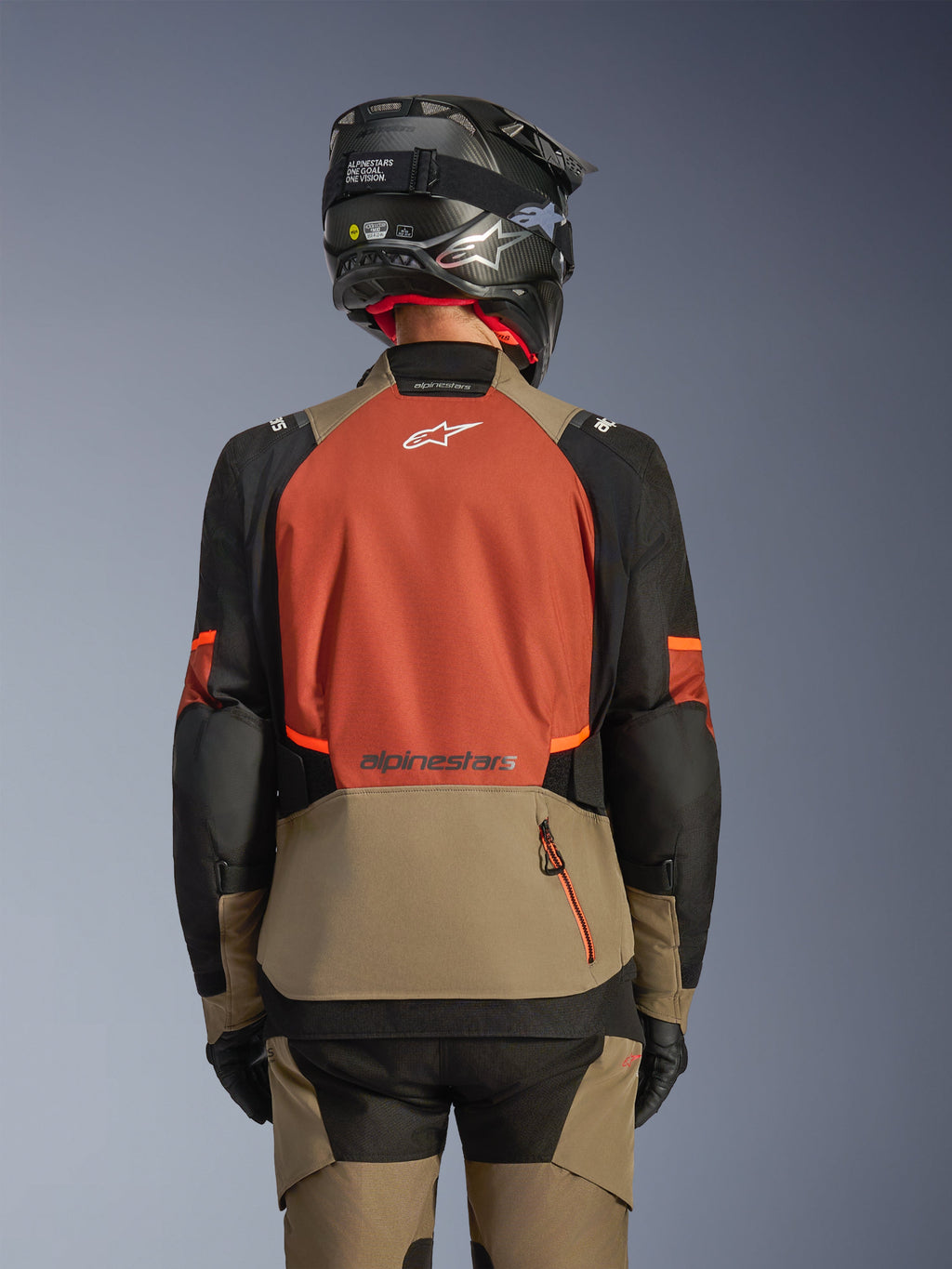 Bagsidevisning af Alpinestars Andes V4 Drystar® jakken i Walnut Rust Black, adventure touring-jakke med et stort rustfarvet rygpanel og hvidt logo, valnøddefarvet underdel med lodret lynlåslomme, sorte ærmer med orange detaljer, stylet med matchende bukser og en sort hjelm til kørsel i al slags vejr.
