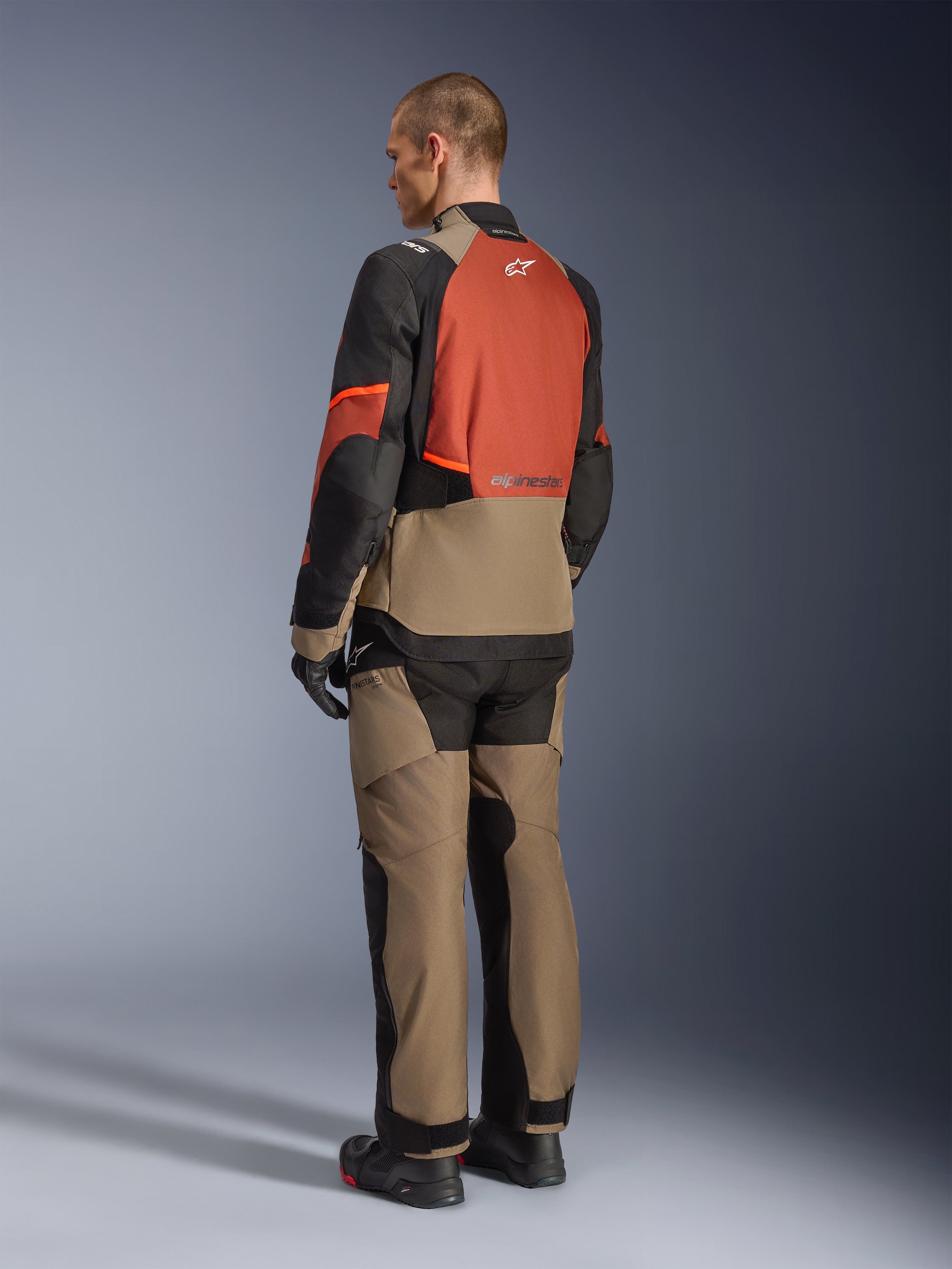 Alpinestars Andes V4 Drystar®-jakke i Walnut Rust Black, model set bagfra iført matchende tekstilbukser, sorte handsker og støvler, med et teknisk design med flere paneler til adventure touring og Alpinestars-branding.