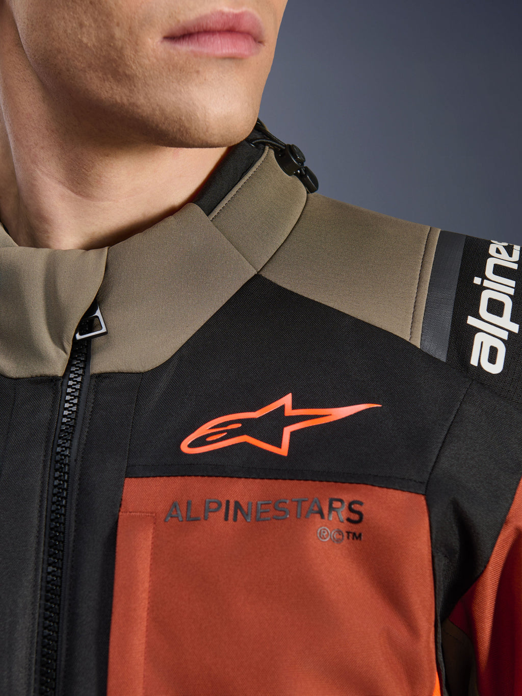 Alpinestars Andes V4 Drystar® jakke i Walnut Rust Black, nærbillede af øvre bryst og skulder, med orange A-star logo på sort panel og Alpinestars-branding på rustfarvet sektion, detalje på adventure motorcykeludstyr