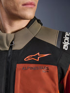 Alpinestars Andes V4 Drystar® jakke i Walnut Rust Black, nærbillede af øvre bryst og skulder, med orange A-star logo på sort panel og Alpinestars-branding på rustfarvet sektion, detalje på adventure motorcykeludstyr