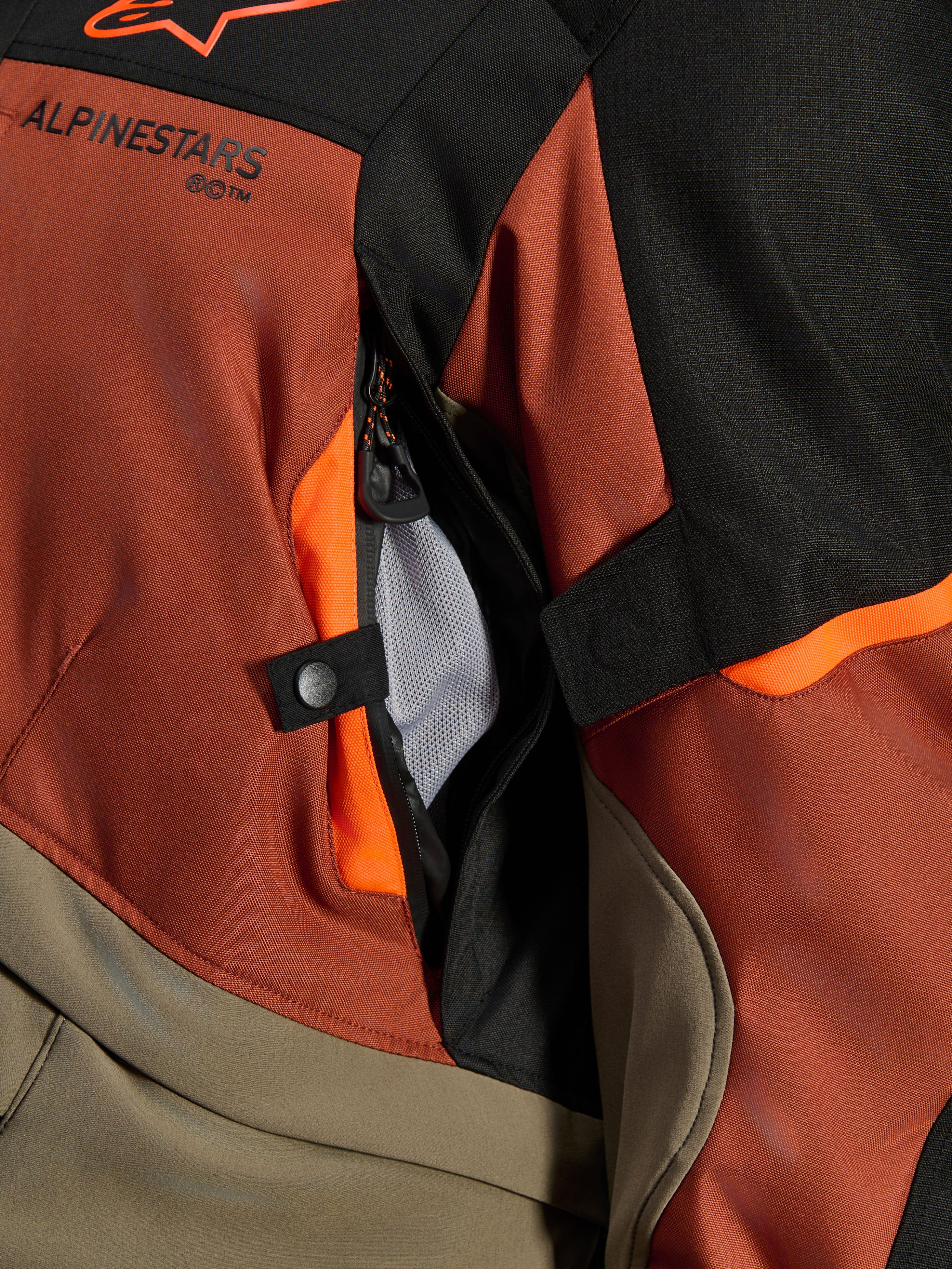 Alpinestars Andes V4 Drystar® jakke, Walnut Rust Black, nærbillede af direkte ventilationsåbning med mesh-foring, slidstærkt tekstilmateriale med orange detaljer, trykknap og Alpinestars-logodetalje