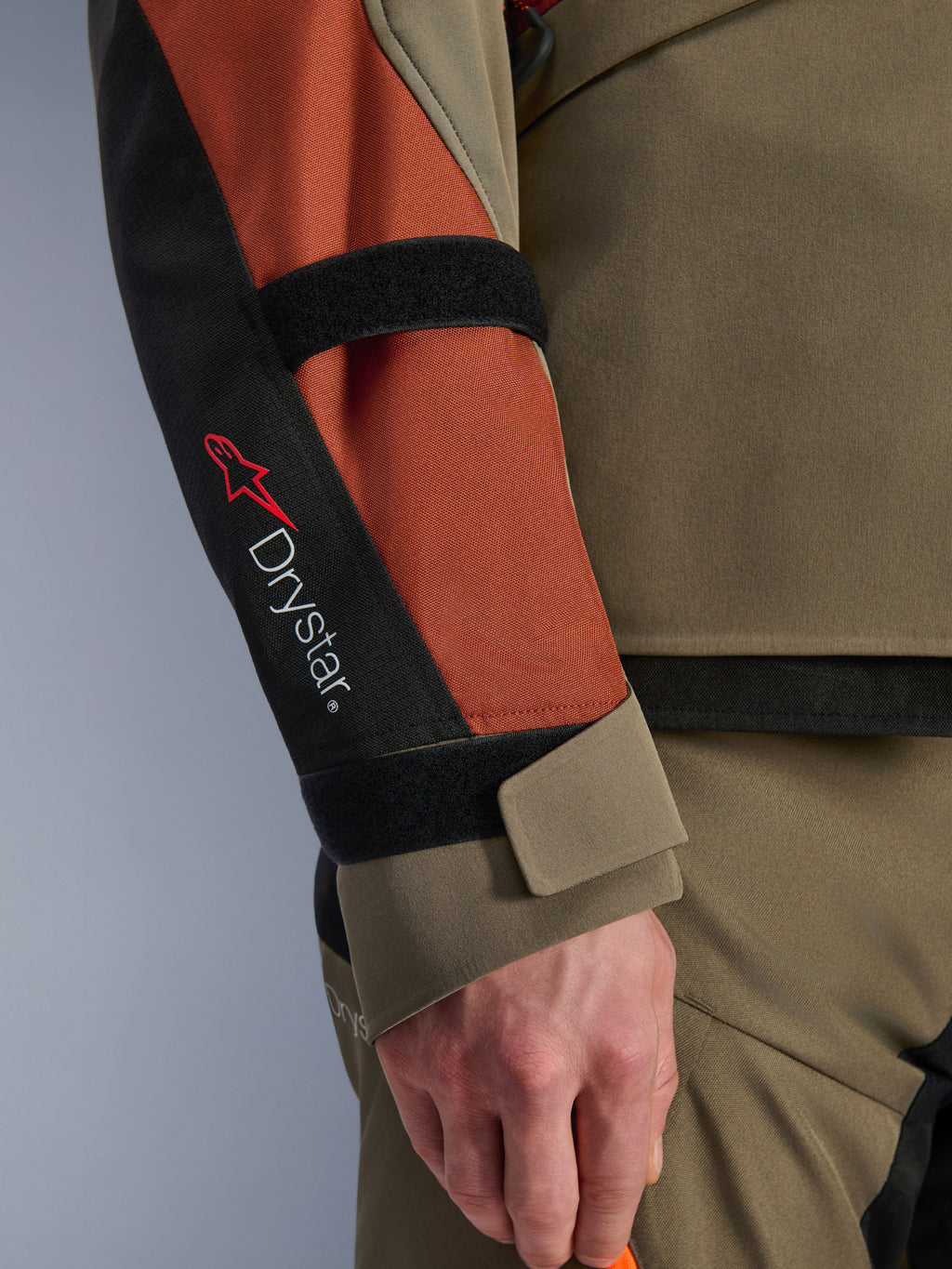 Alpinestars Andes V4 Drystar® jakke, motorcykeljakke, Walnut Rust Black, nærbillede af ærmet med Drystar®-branding og rødt stjernelogo, med justerbare velcrostropper på underarm og håndled, slidstærkt adventure touring-tekstildesign.