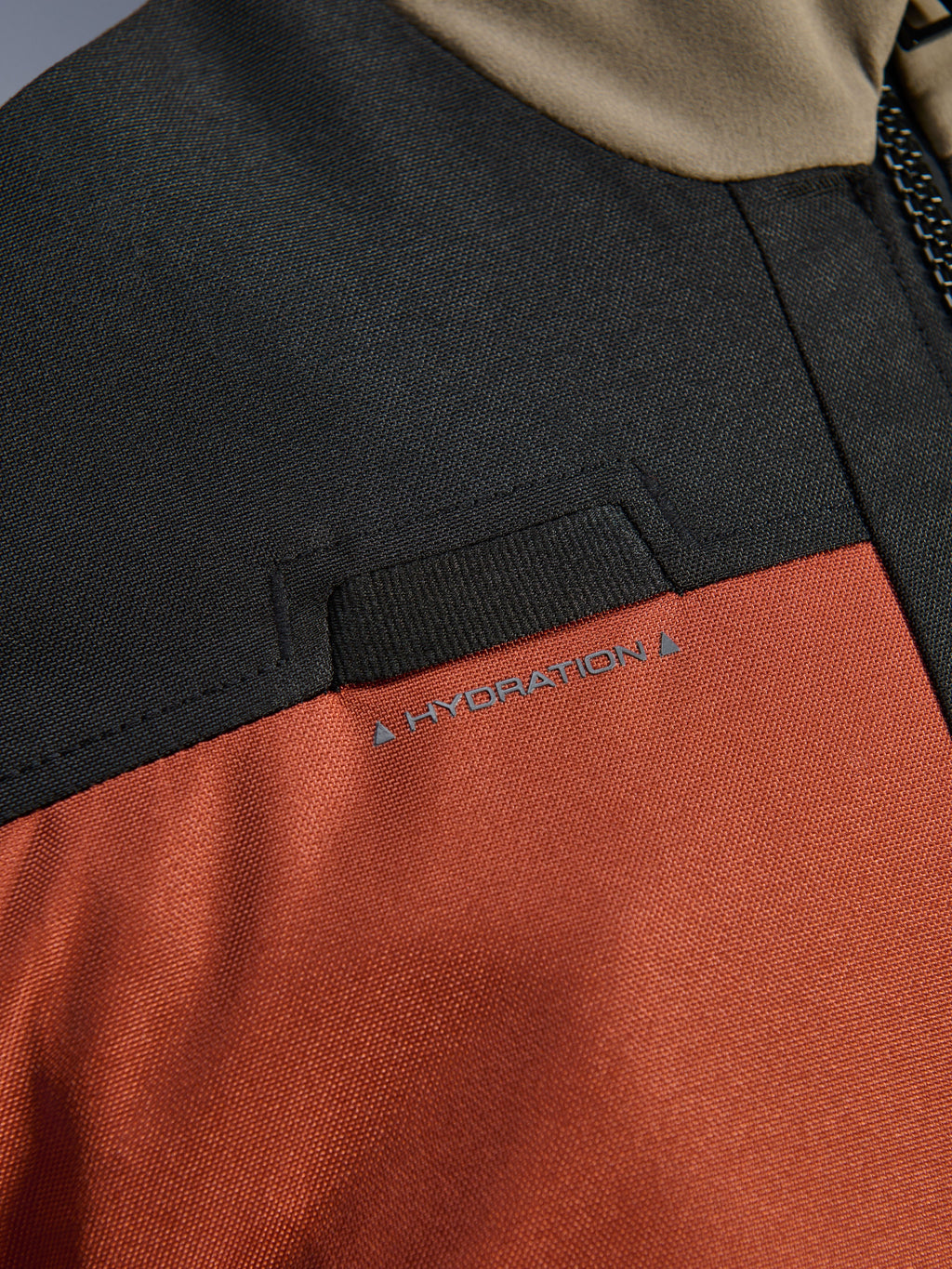 Nærbillede af detaljer på Alpinestars Andes V4 Drystar® Jakken i Walnut Rust Black, der fremhæver den integrerede løkke til hydreringsslange på brystet og den slidstærke ripstop-tekstilkonstruktion.