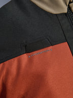 Nærbillede af detaljer på Alpinestars Andes V4 Drystar® Jakken i Walnut Rust Black, der fremhæver den integrerede løkke til hydreringsslange på brystet og den slidstærke ripstop-tekstilkonstruktion.