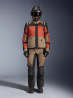 Adventure-rytter iført Alpinestars Andes V4 Drystar® jakke i Walnut Rust Black, stylet med matchende adventure-bukser, sort hjelm med røde detaljer og goggles samt sorte handsker, der viser et komplet touring-outfit til al slags vejr.