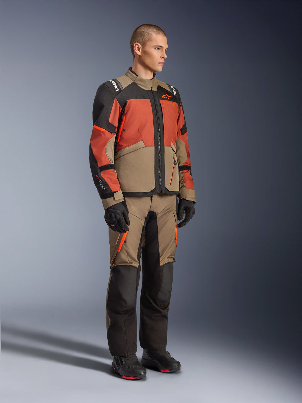 Alpinestars Andes V4 Drystar® Jakke, adventure touring-jakke, Walnut Rust Black, bæres med matchende bukser og sorte støvler, med et farveopdelt design i tan, rust og sort, slidstærk tekstilkonstruktion med synlige lynlåse og Alpinestars-logoer.