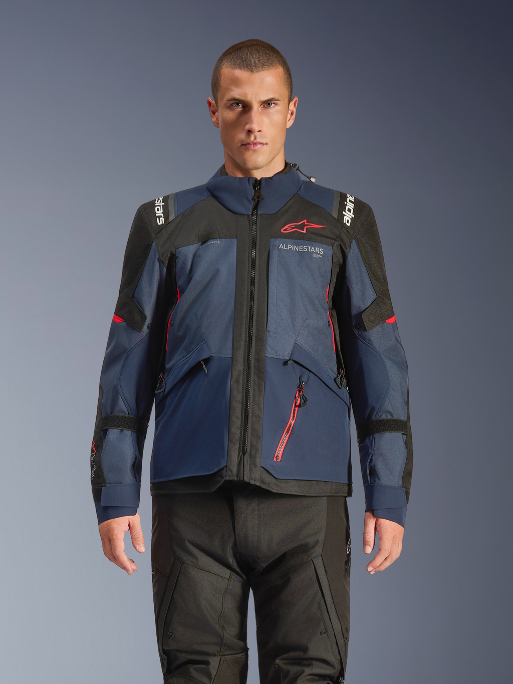 Alpinestars Andes V4 Drystar® jakke, adventure-motorcykeljakke, Night Navy og Mood Indigo med sorte paneler, båret af model med sorte kørebukser, rødt Alpinestars-logo på brystet og rød lynlåsdetalje, holdbar tekstilkonstruktion til touring i al slags vejr.