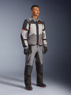Male model wearing Alpinestars Andes V4 Drystar® Jacket and matching adventure pants, Dark Gray, Ice Gray, Black, and Bright Red, paired with black motorcycle gloves and boots, technical all-weather riding gear with a modern multi-panel design.