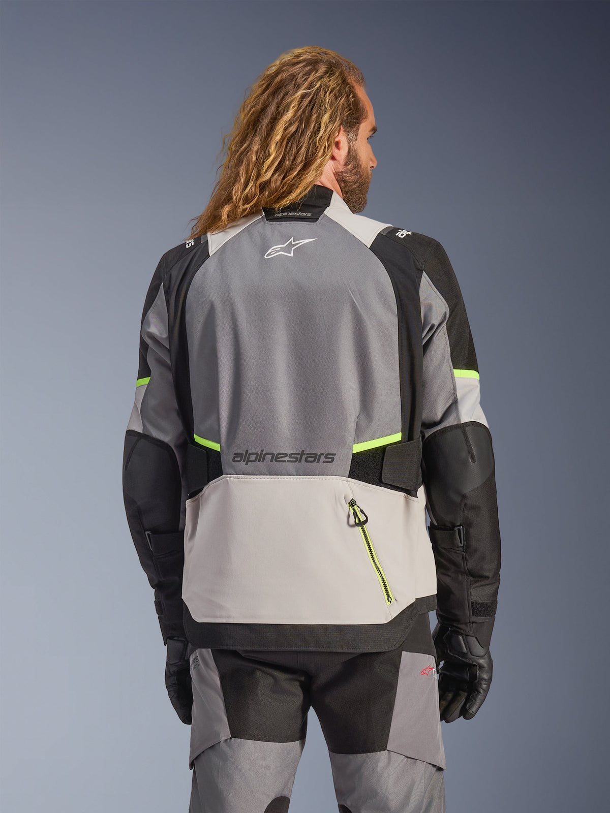 Alpinestars Andes V4 Drystar® jakke, adventure-motorcykeljakke set bagfra i mørkegrå, isgrå og sort med fluorescerende gule fluo-detaljer, med forstærkede tekstilpaneler og Alpinestars-branding, båret med matchende kørebukser og sorte handsker