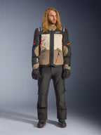 Alpinestars Andes V4 Drystar®-jakke, Walnut Mastic Black, båret med sorte motorcykelbukser og handsker, med et multi-panel adventure-design med orange detaljer og Alpinestars-branding, teknisk tekstiludstyr til kørsel i al slags vejr