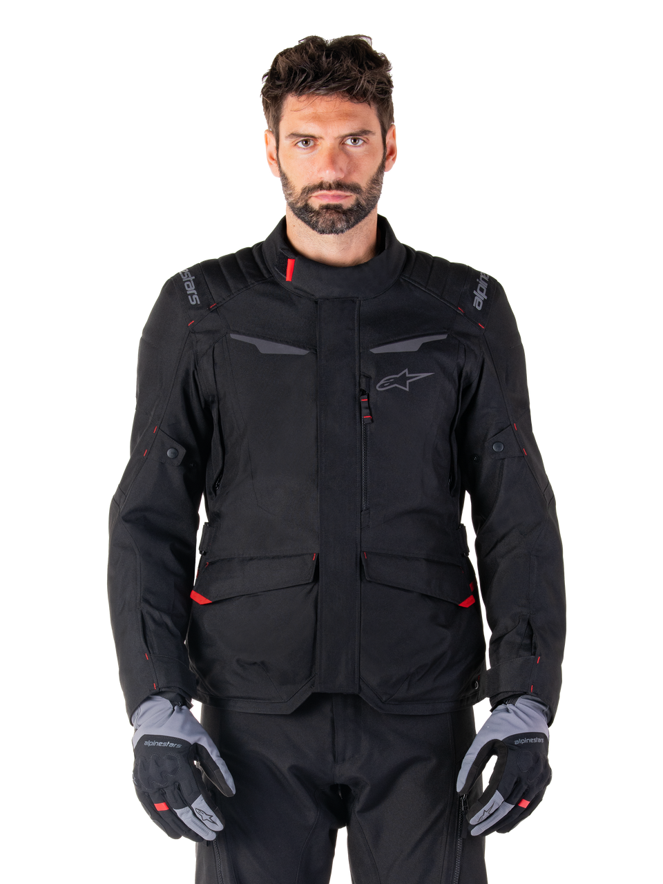 Alpinestars ST-1 Waterproof Jacket, sort adventure touring-motorcykeljakke, båret af en mandlig model med matchende sorte bukser og grå/sorte handsker, med minimalistisk styling, Alpinestars-branding på skuldrene, store cargo-lommer foran med røde detaljer og ergonomisk konstruktion til touring under alle vejrforhold.