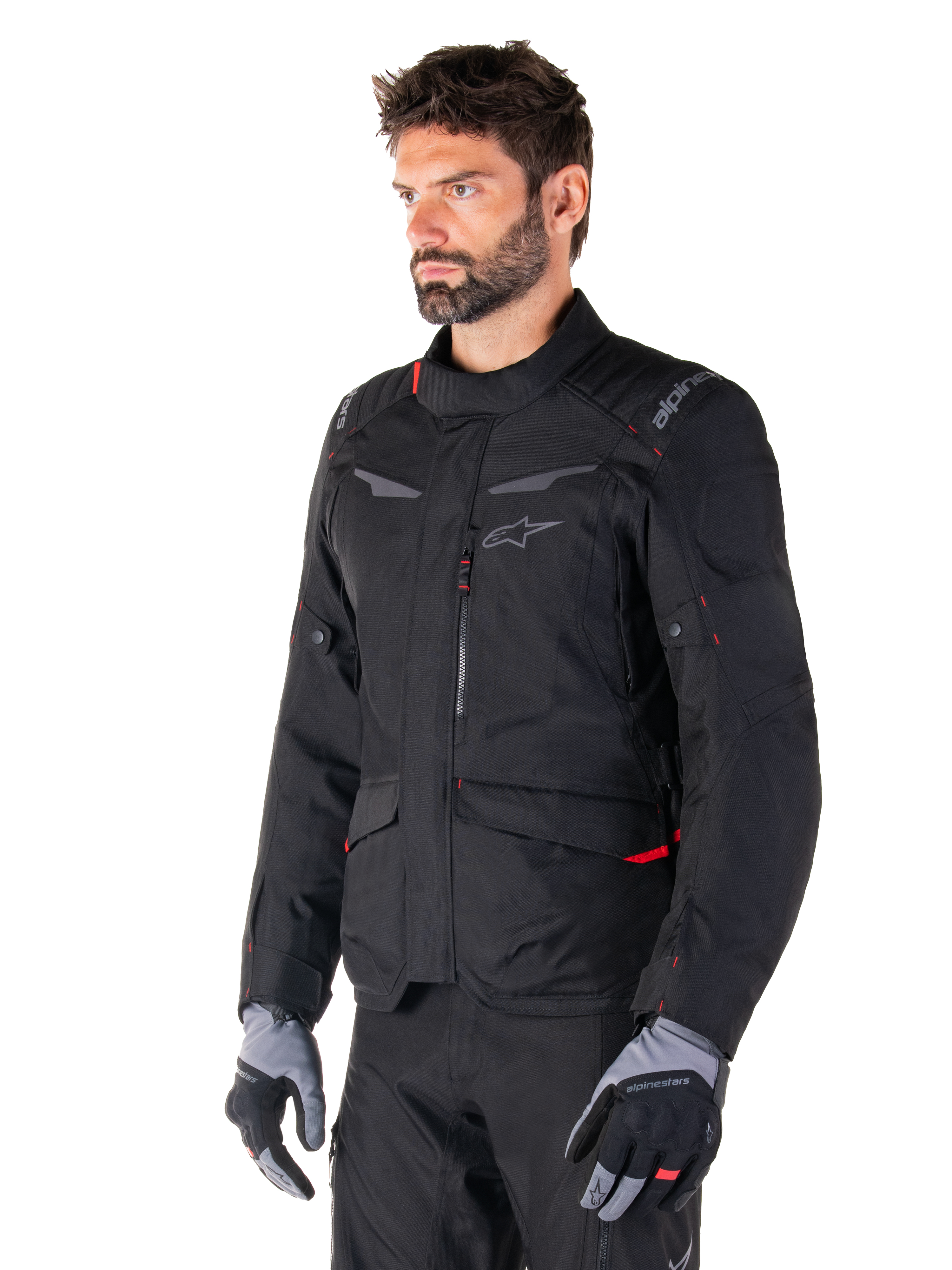 Alpinestars ST-1 Waterproof Jacket, Black with red accents, worn by a male rider with grey and black gloves, featuring a minimalist adventure touring design, cargo pockets, and subtle Alpinestars branding.