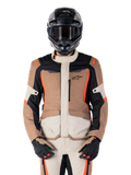 Alpinestars ST-1 vandtæt jakke, mørk khaki sand sort rød fluo, båret af en kører med sort hjelm og handsker, adventure touring-udstyr med beige og brune paneler og klare røde fluo-detaljer, set forfra på en hvid baggrund.