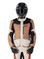 Alpinestars ST-1 vandtæt jakke, mørk khaki sand sort rød fluo, båret af en kører med sort hjelm og handsker, adventure touring-udstyr med beige og brune paneler og klare røde fluo-detaljer, set forfra på en hvid baggrund.