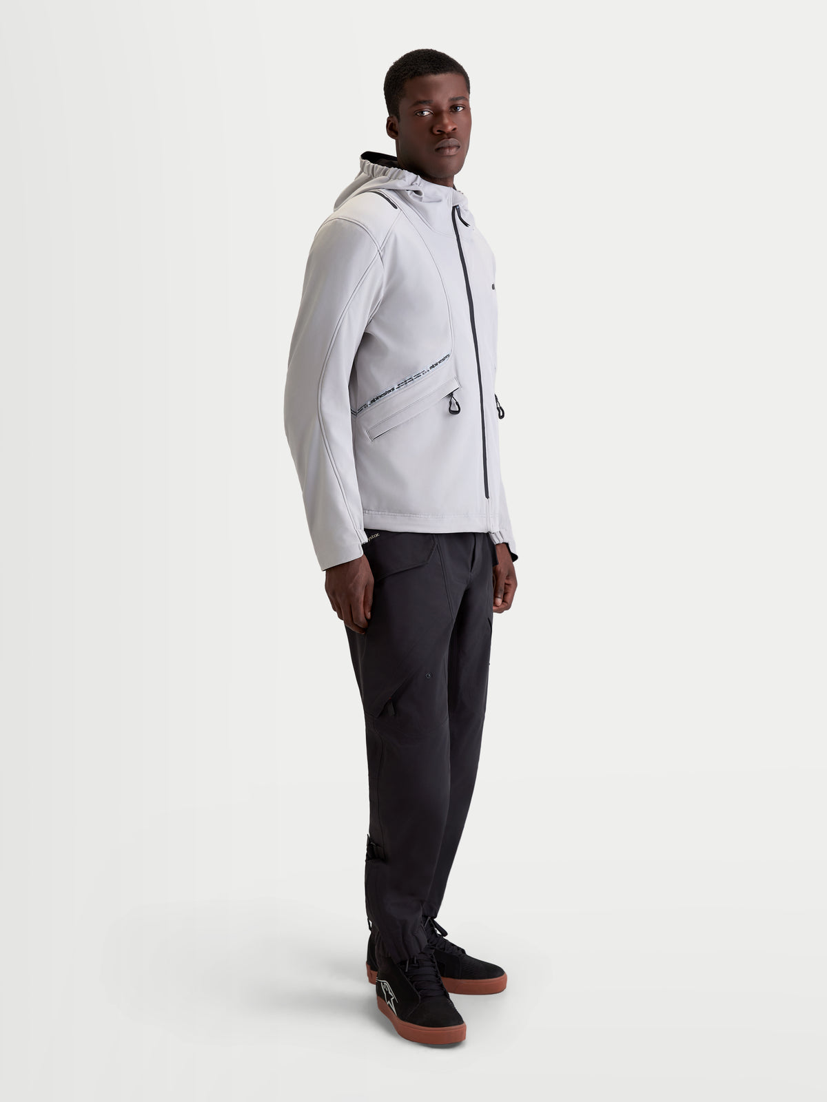Alpinestars C 5 Drystar Jakke, herre urban contemporary motorcykeljakke i lys grå og sort, sideprofil af model iført matchende mørke bukser og køresko, vandtæt 2-lags softshell-konstruktion med integreret hætte