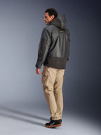 Man wearing the Alpinestars Mospher Waterproof Jacket in Black, back and side profile view, paired with tan cargo pants and black sneakers. Features a hooded parka design with ripstop fabric, Alpinestars branding on the sleeve, and a modern urban motorcycle style.