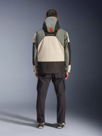 Set bagfra af en kører iført Alpinestars Mospher Waterproof Jacket i Fur Gray Black Ice, taktisk inspireret parka med grå, sorte og cremefarvede farveblokke, har en hætte med orange remdetalje, parret med sorte cargobukser.