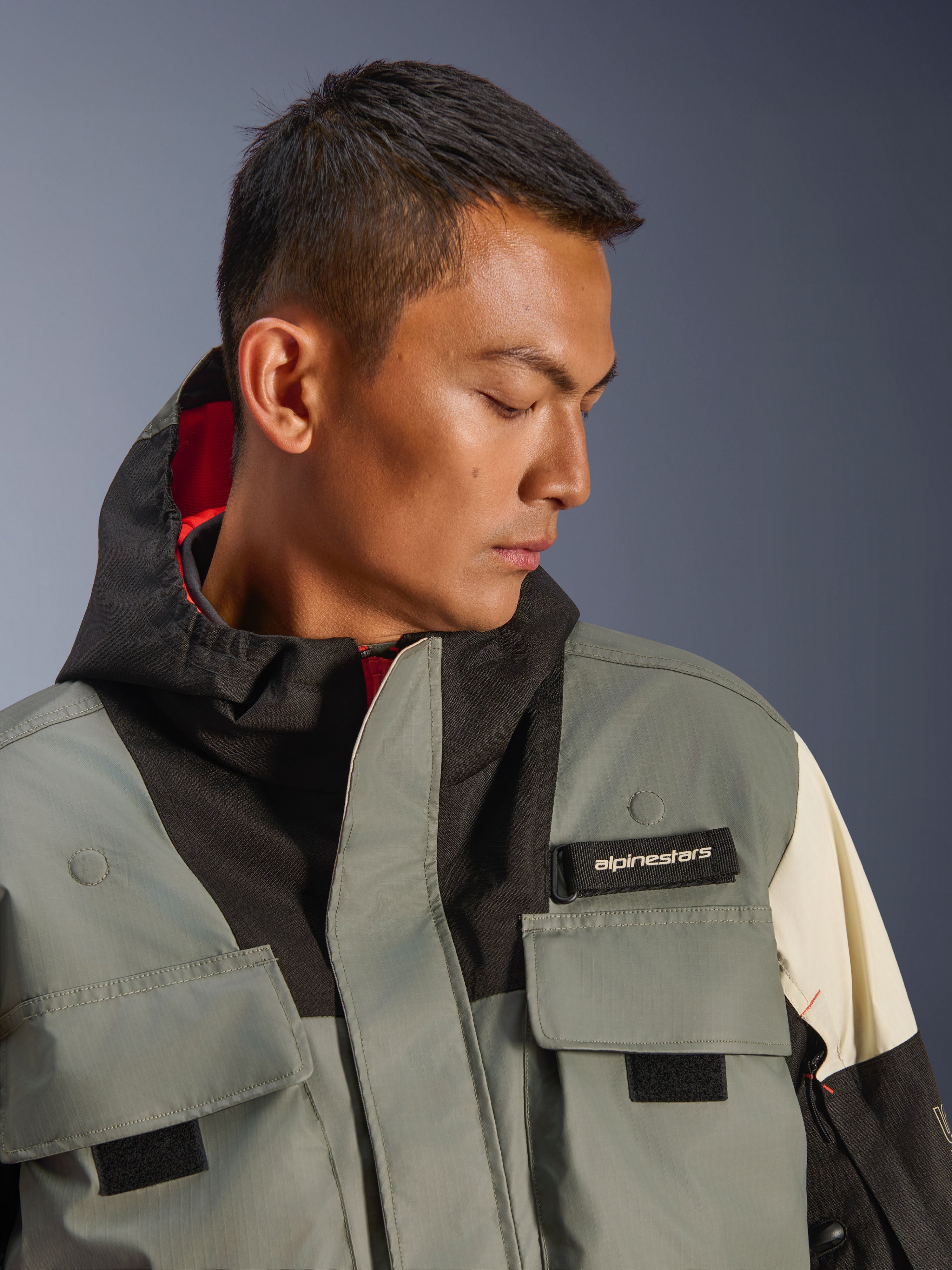 Alpinestars Mospher WP-jakke, vandtæt motorcykelparka, Fur Gray Black Ice, nærbillede af model iført jakke med hætte med funktionelle lommer, sort Alpinestars-logofane og taktisk design med rødt indvendigt for