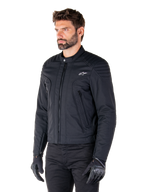 Alpinestars Clayton WR Jakke, sort, urban motorcykeljakke i tekstil med quiltede detaljer på skuldre og underarme, slim-fit design, mat finish, båret af en kører med sorte handsker.
