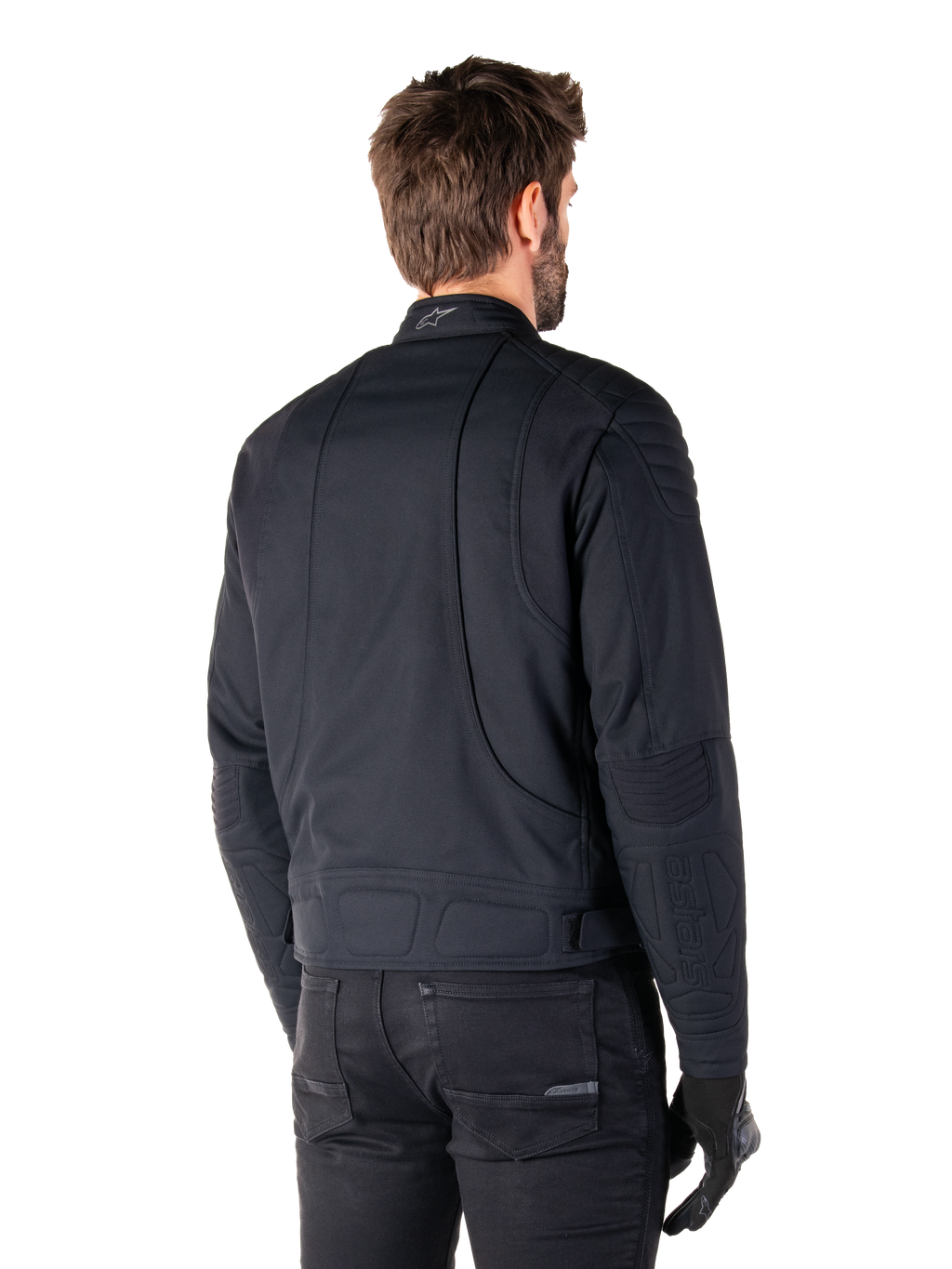Alpinestars Clayton WR Jakke i sort, trekvart visning bagfra på en mandlig model, urban motorcykeljakke med quiltet polstring på skuldre og albuer, tekniske syninger og reflekterende logo på kraven, stylet med sorte bukser og handsker.